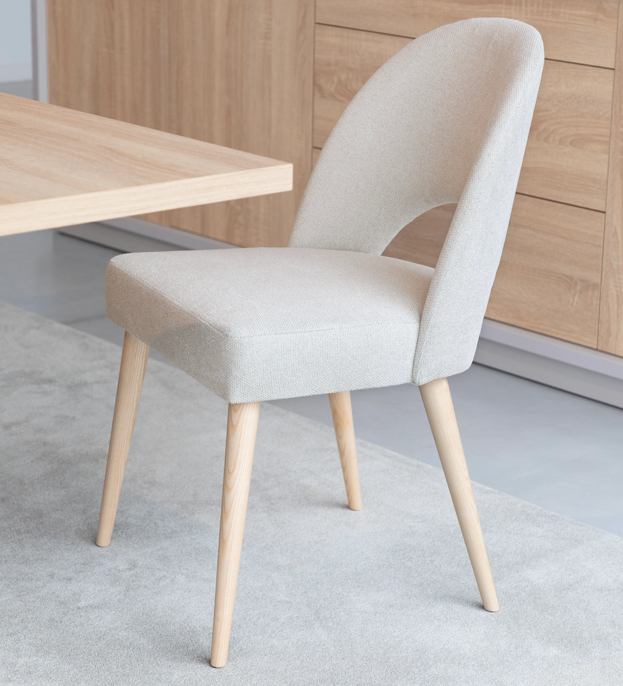 Chair upholstered in beige fabric, with natural colored wooden legs.