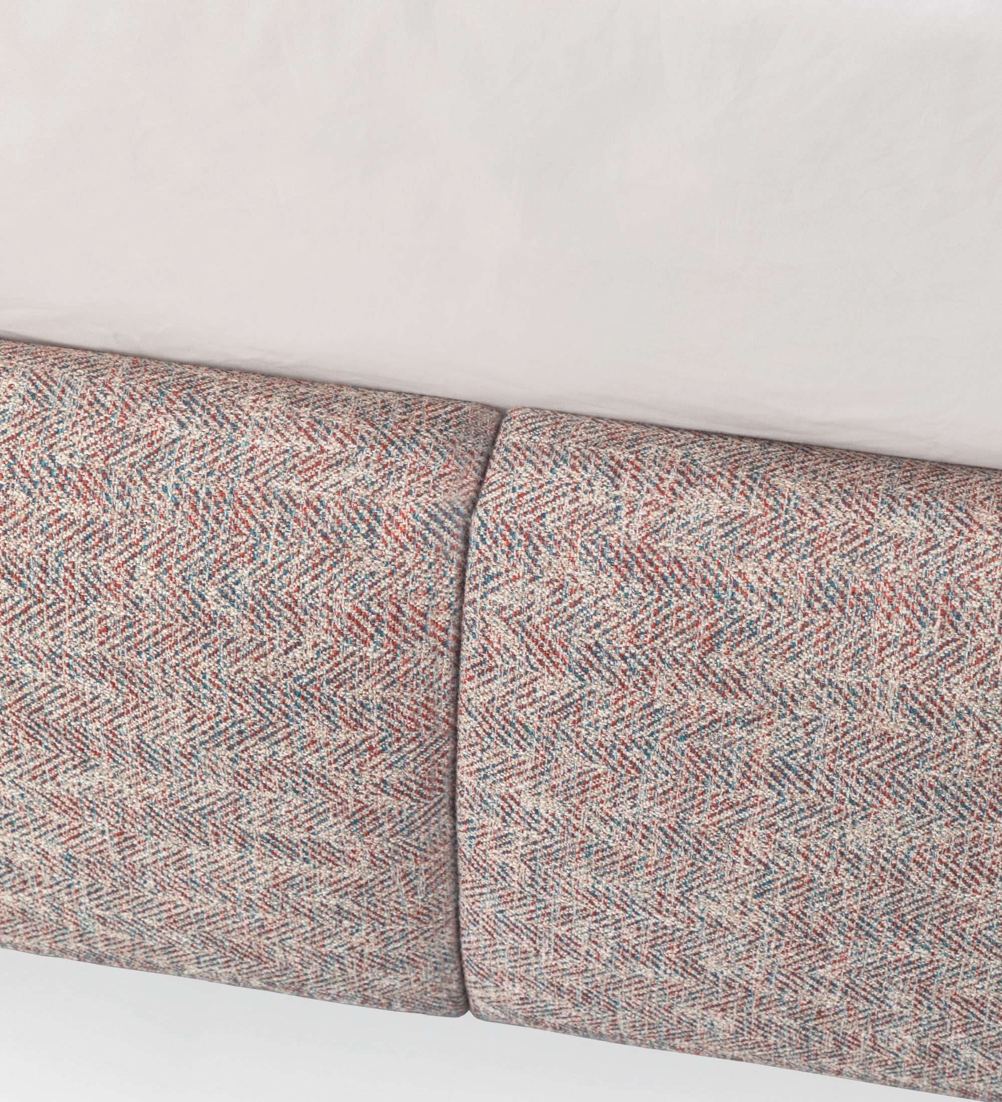 Double bed with short headboard, upholstered in multicolored fabric, primarily red and blue.