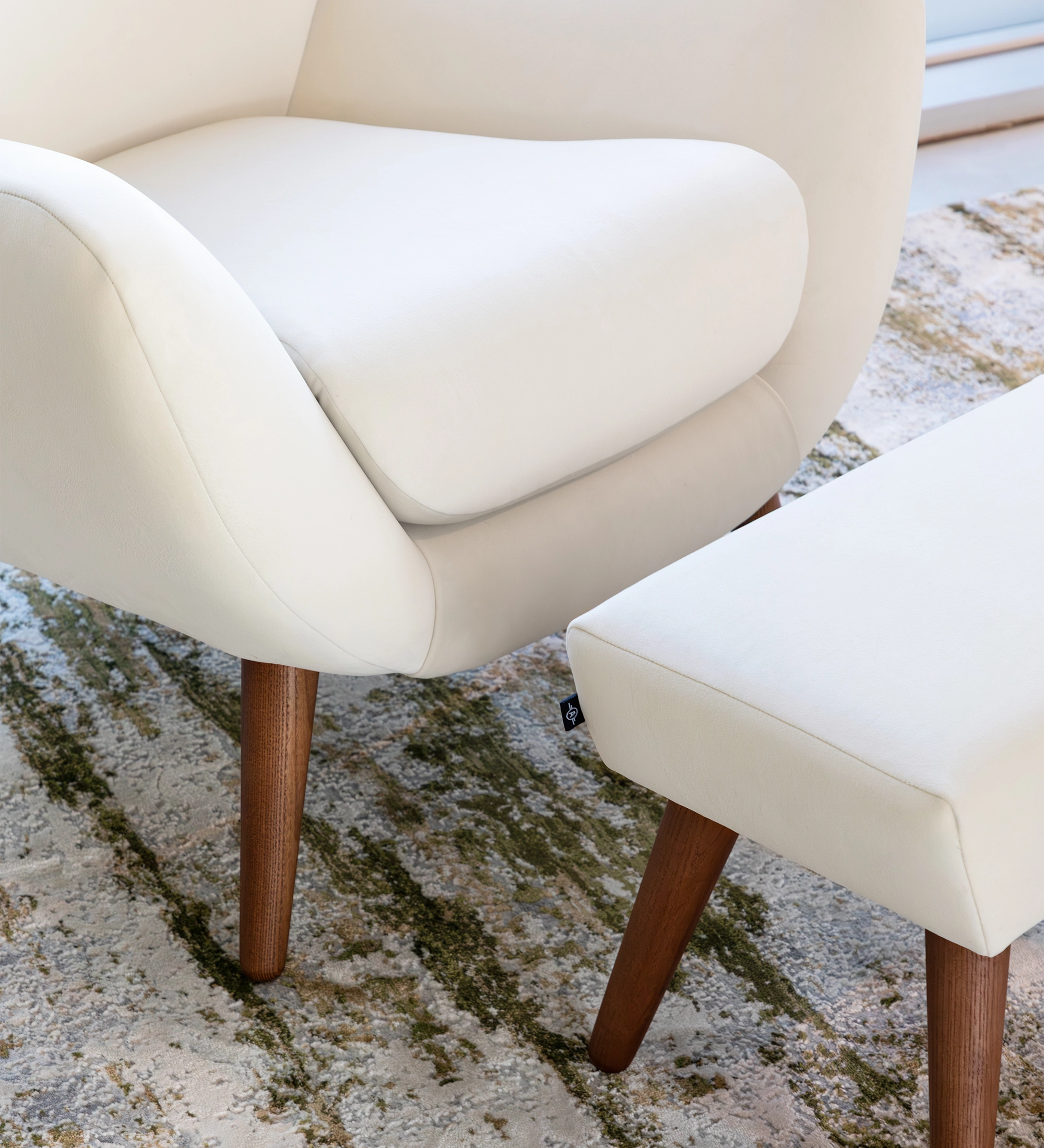 Fauteuil Oslo revêtu de tissu couleur perle avec pieds en frêne teinté noyer.
