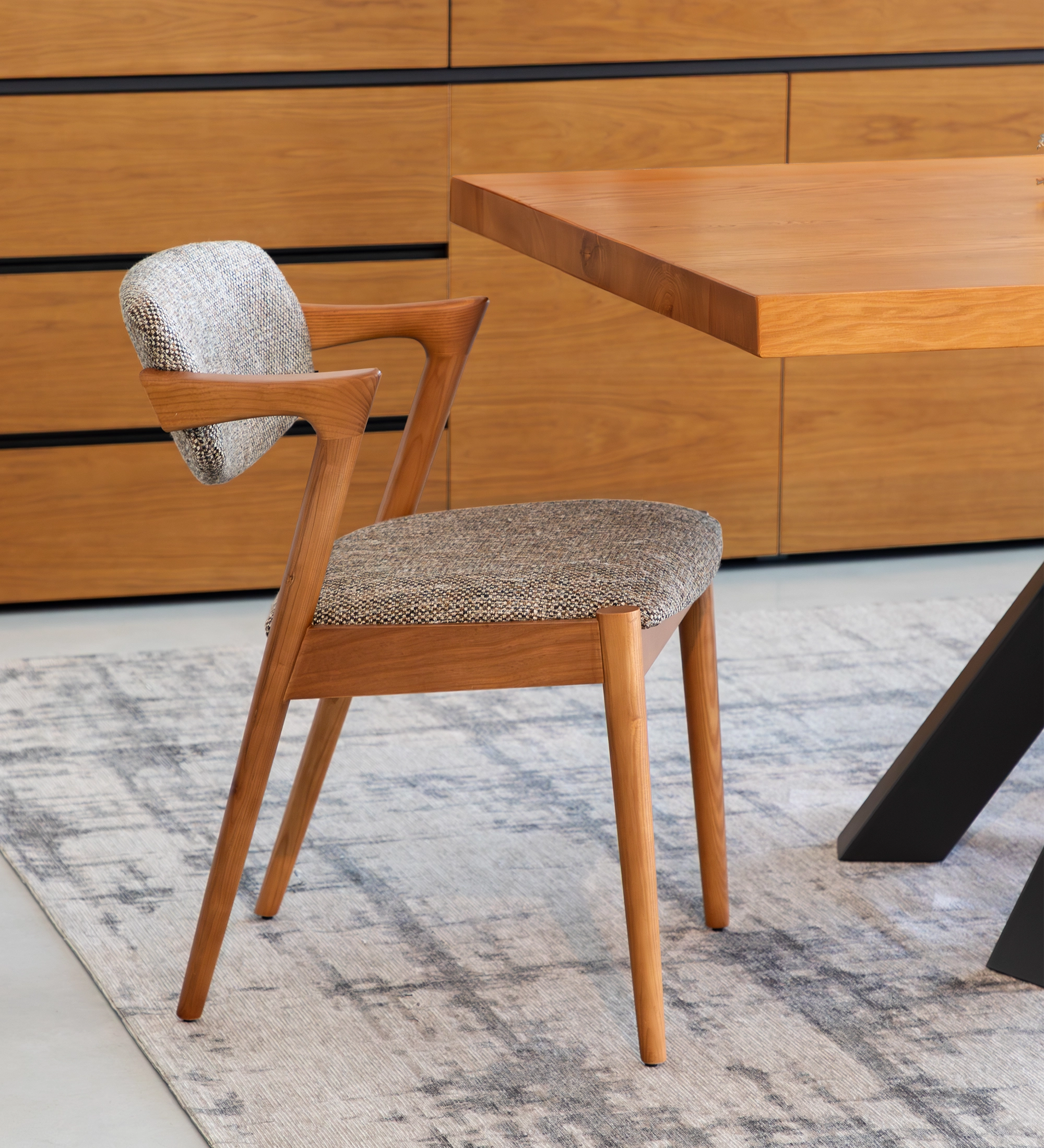 Chaise en frêne couleur miel, avec assise et dossier rembourrés en tissu multicolore, principalement dans les tons bruns et beige.