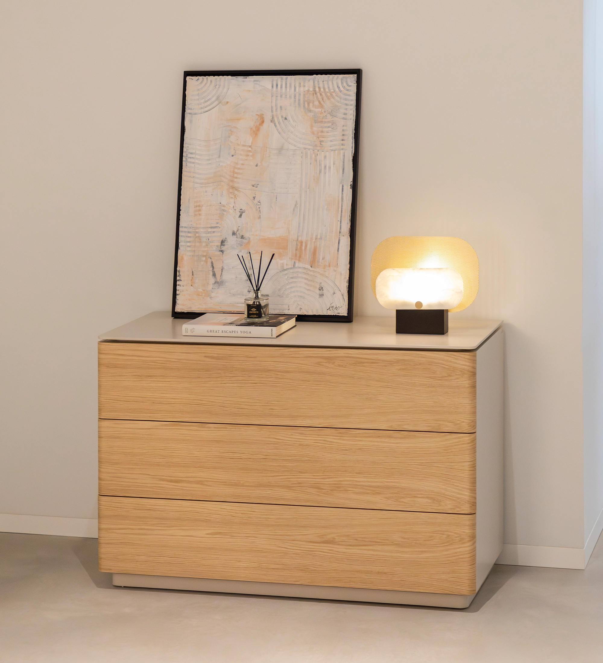 Cómoda Geneve em madeira clara com três gavetas, candeeiro e quadro no tampo