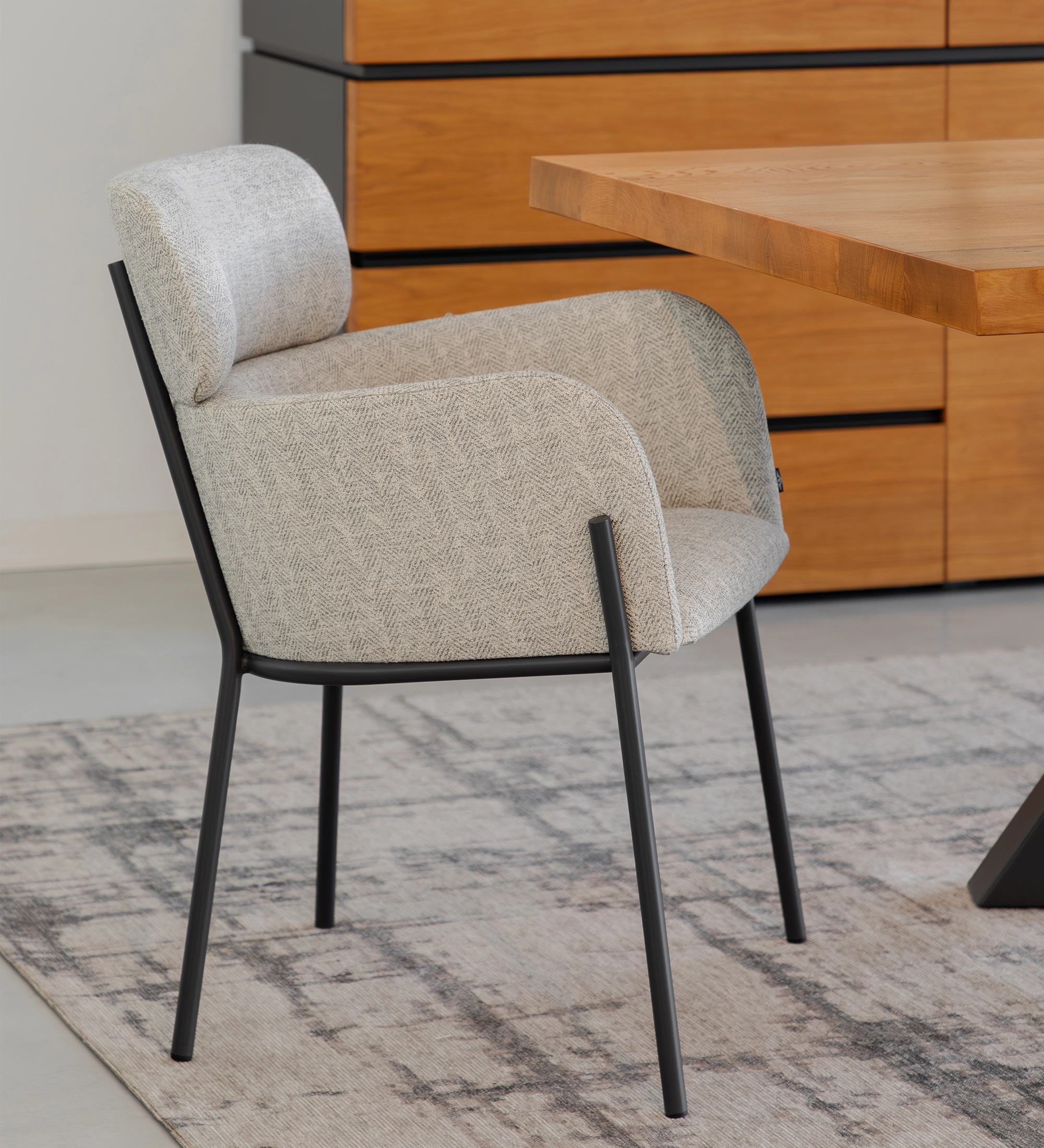 Silla Cannes tapizada gris claro con patas metálicas negras junto a mesa de madera