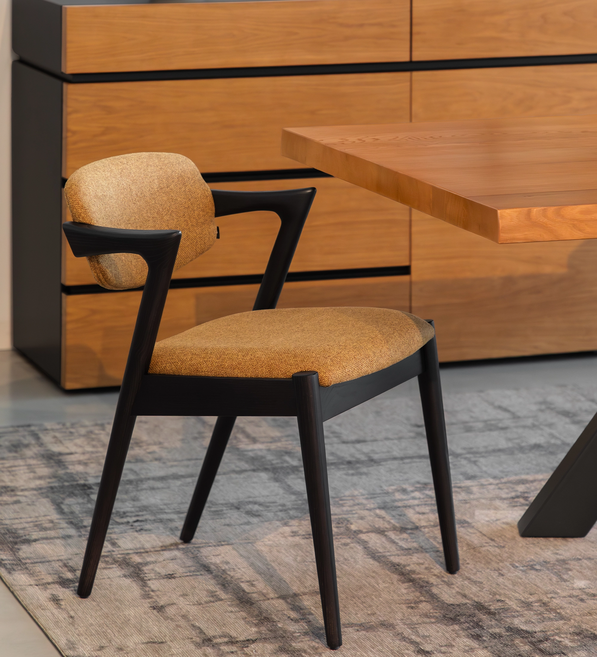 Silla Elba de comedor tapizada en mostaza con estructura negra junto a mesa de madera