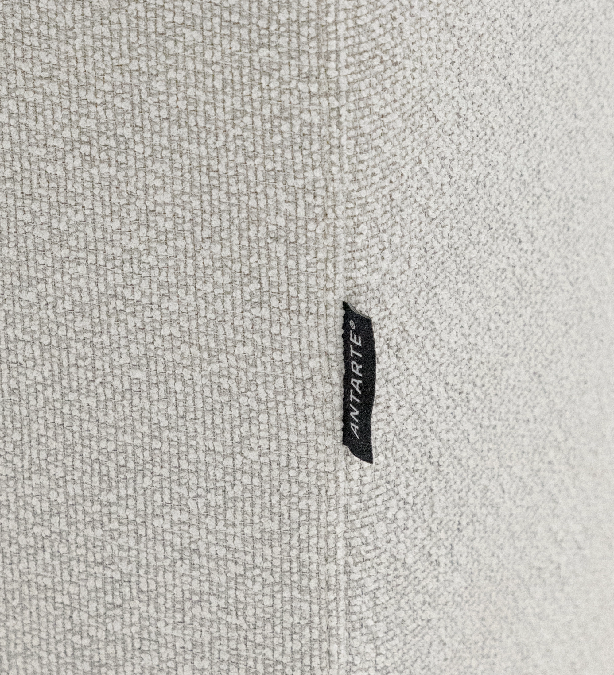 Primer plano del sofá Lagos en tejido beige claro con etiqueta negra 'ANTARTE'.