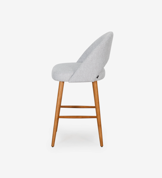 Stool with light grey fabric upholstered, with honey-colored wooden feet.