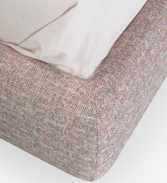 Double bed with short headboard, upholstered in multicolored fabric, primarily red and blue.