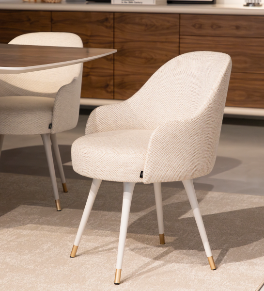 Beige fabric upholstered swivel chair with pearl lacquered feet and gold detailing.