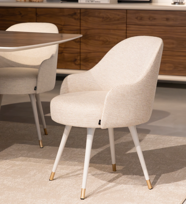 Beige fabric upholstered swivel chair with pearl lacquered feet and gold detailing.