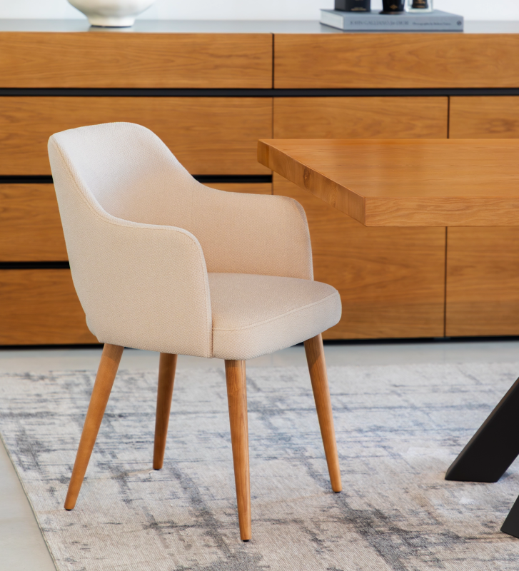 Chaise avec accoudoirs, revêtue de tissu beige, pieds en bois couleur miel.
