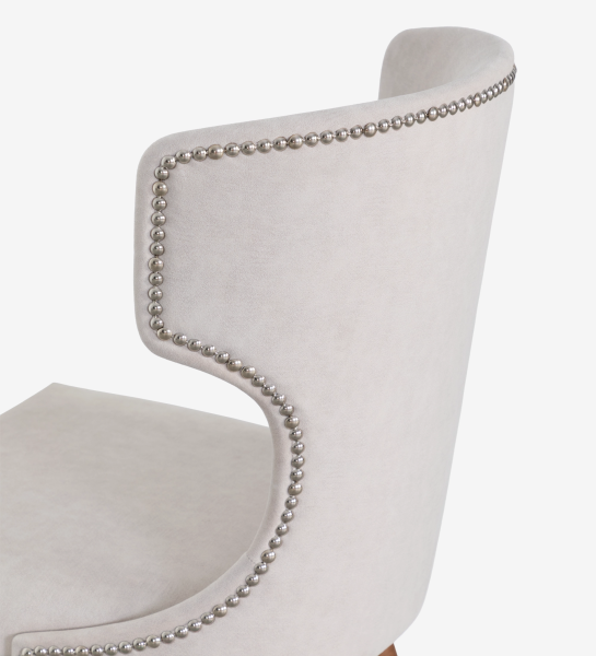 Silla tapizada en tela color perla, con tachuelas plateadas en el respaldo y patas de fresno en tono nogal.