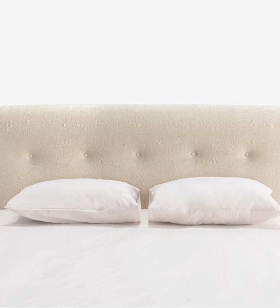 Cama doble con cabecero corto, tapizada en tela beige.