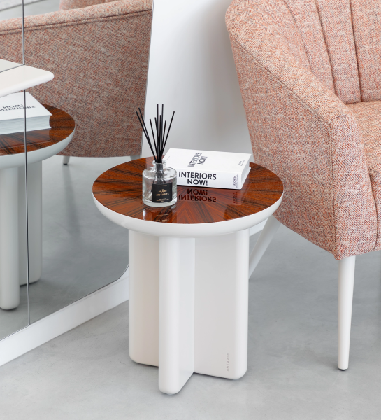 Mesa Auxiliar Mónaco blanca con tablero de madera y difusor, junto a butaca rosa