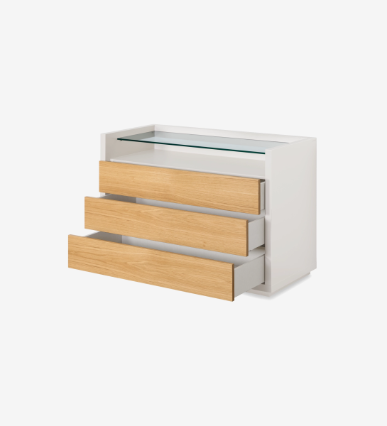 Commode blanche avec trois tiroirs en bois clair et plateau supérieur en verre