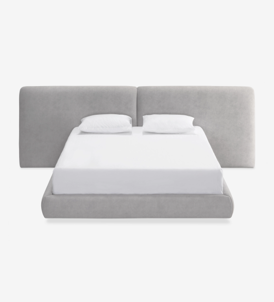 Cama doble tapizada gris con cabecero amplio, ropa blanca y dos almohadas