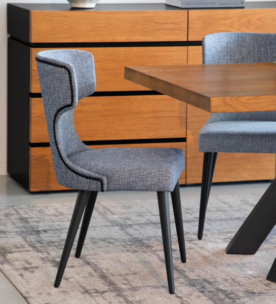 Cadeira Pico estofada azul-cinzento com pernas pretas e pespontos, junto a mesa