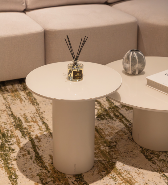 Paris Side Table round cream pedestal with reed diffuser beside beige sofa on patterned rug
