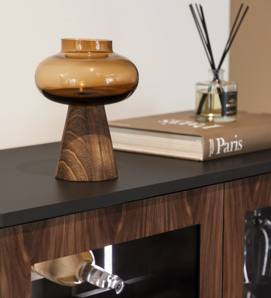 Jarrón Daphne negro con hojas verdes sobre mesa con lámparas colgantes y mandarinas